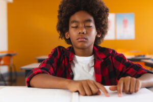 A boy has his eyes closed and trying to figure out the braile letters